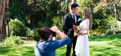 Svatební fotograf na letní zahradě fotí nevěstu s ženichem.